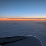 Blick aus dem Flugzeugfenster auf den Sonnenuntergang über einer Wolkendecke.