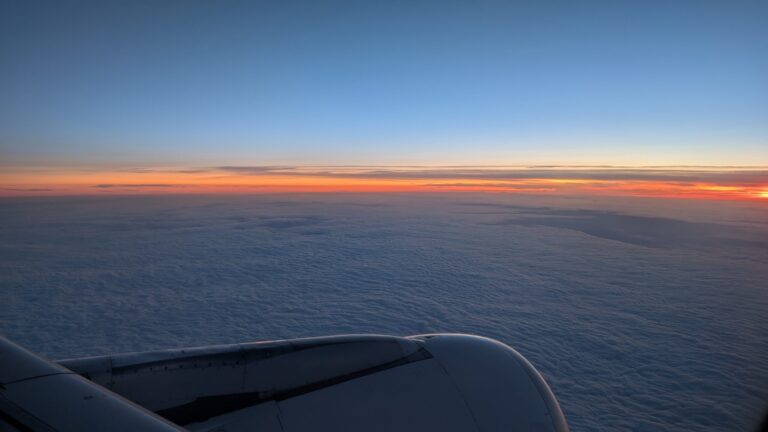 Blick aus dem Flugzeugfenster auf den Sonnenuntergang über einer Wolkendecke.